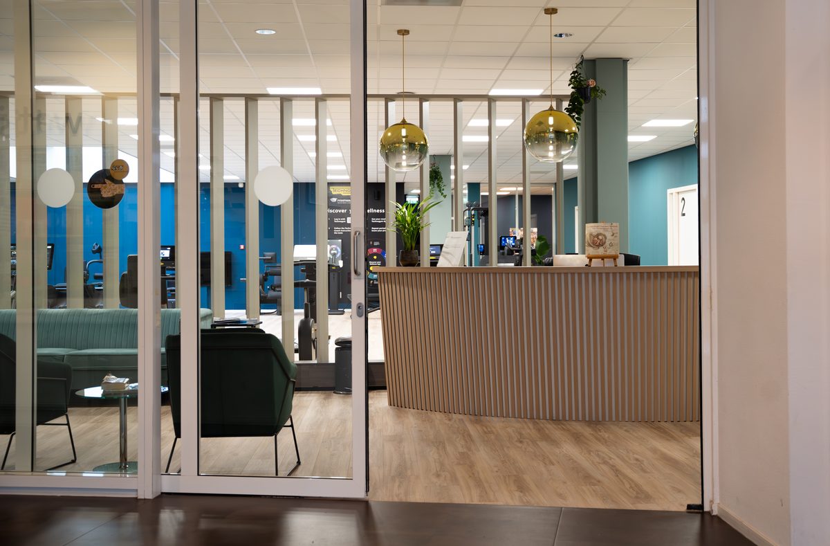 De balie en ontvangstruimte van Fysio Bladel, met de oefenzaal op de achtergrond.